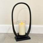 Black arch-shaped candle holder with a white candle on a neutral background