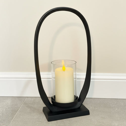 Black arch-shaped candle holder with a white candle on a neutral background