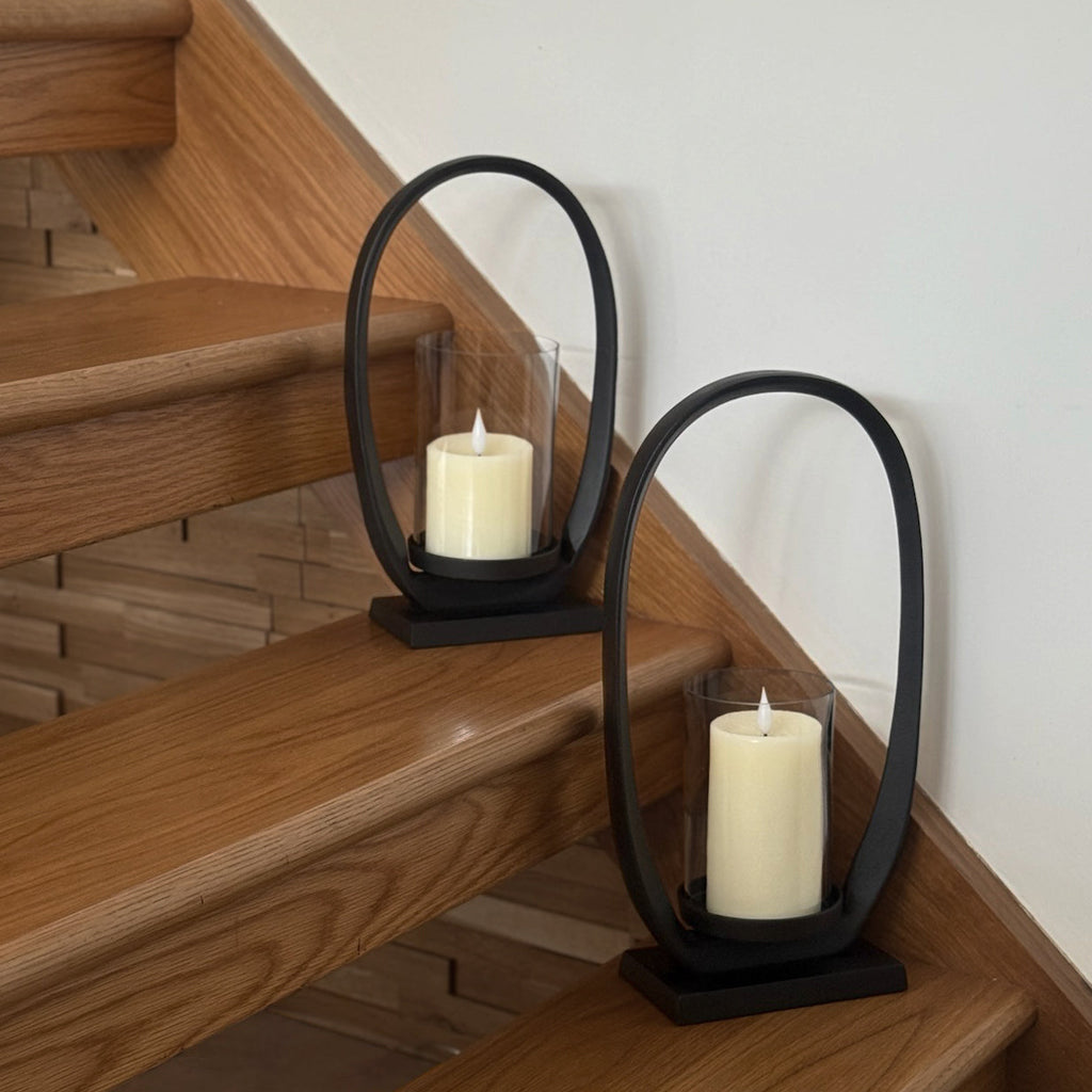 Two black metal candle holders with white candles on wooden stairs.