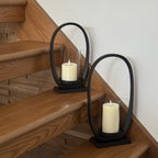 Two black metal candle holders with white candles on wooden stairs.