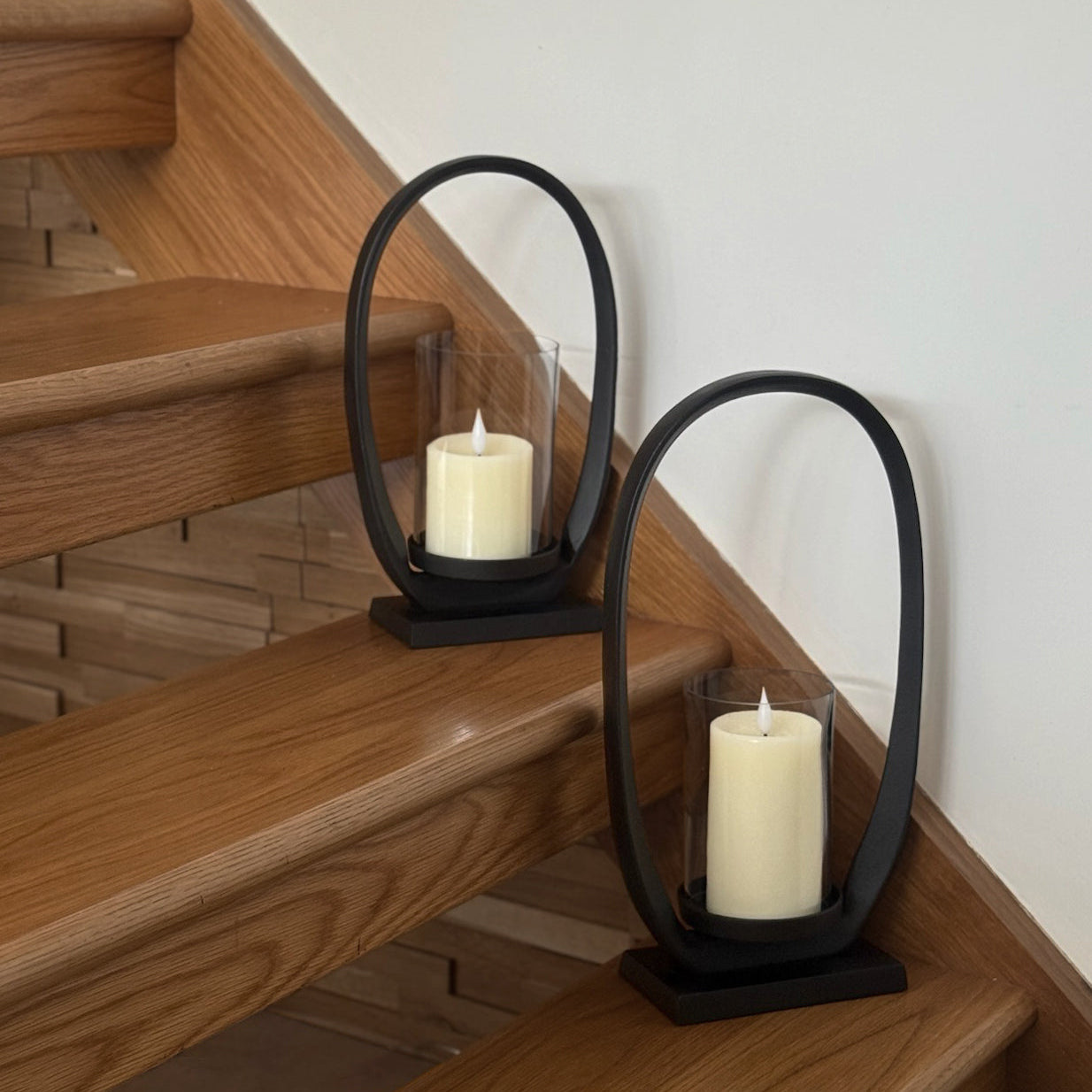 Two black metal candle holders with white candles on wooden stairs.