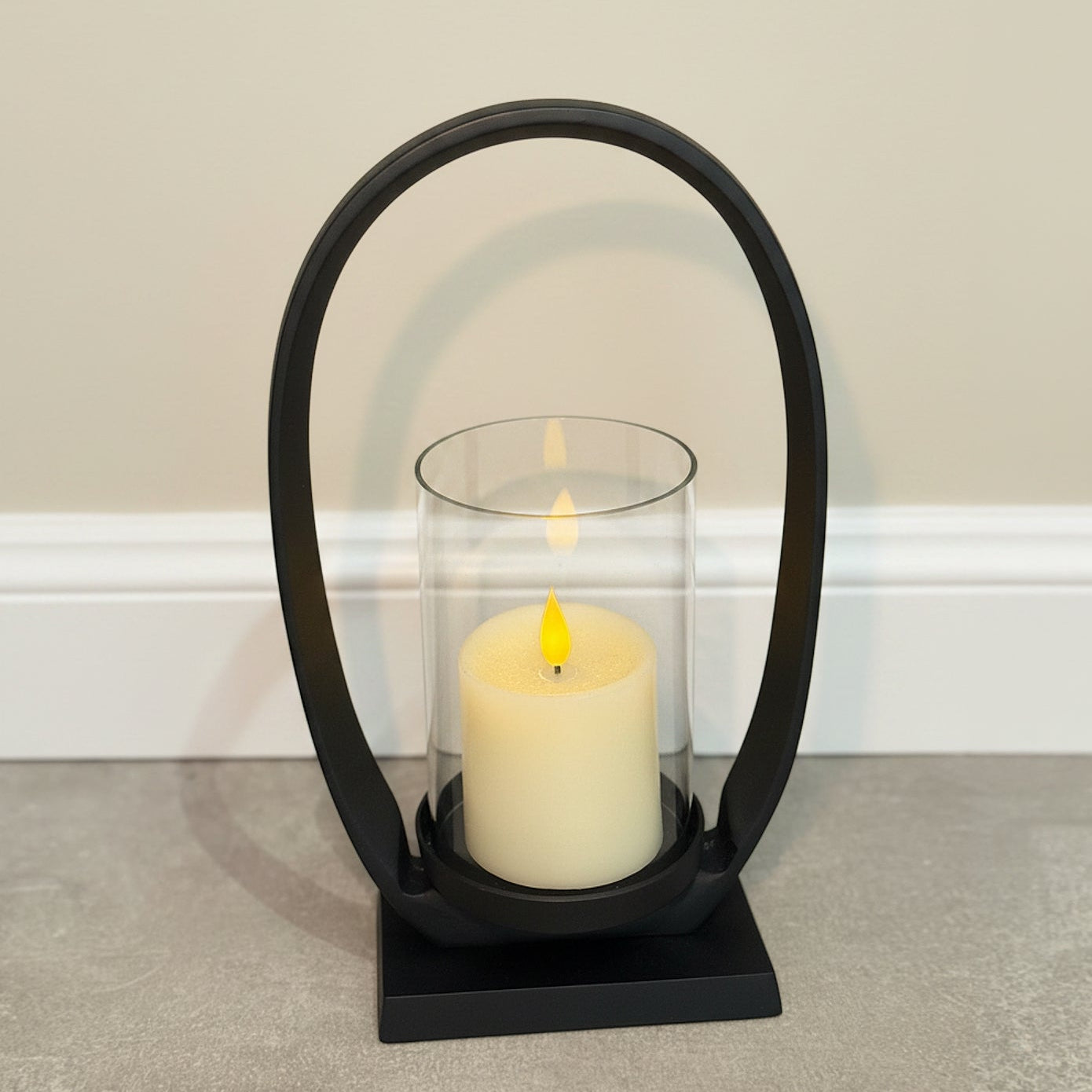 Black lantern with a lit candle inside on a neutral background