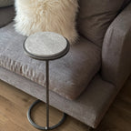 Small round side table with marble top and metal base next to a gray sofa with a fluffy white pillow.