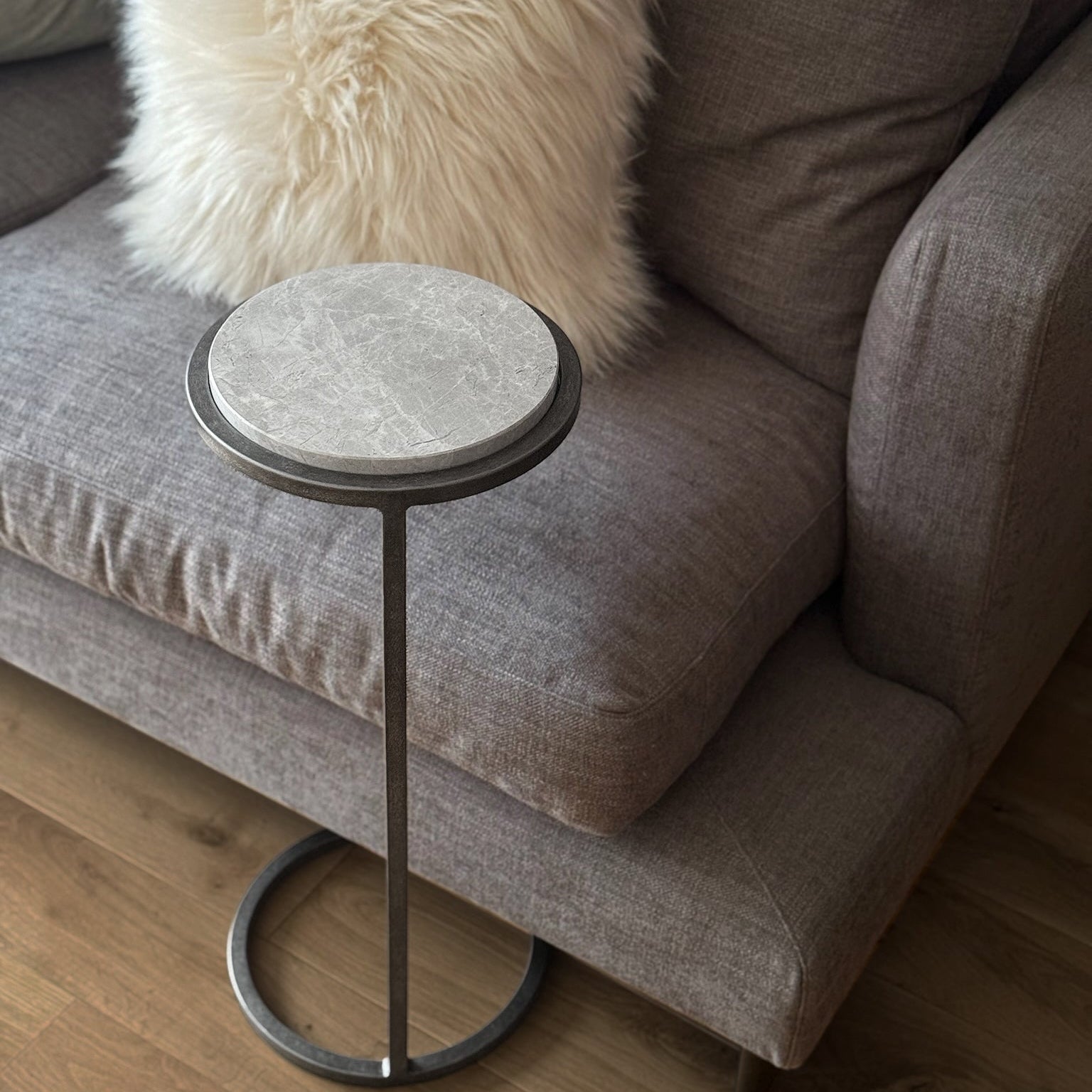 Small round side table with marble top and metal base next to a gray sofa with a fluffy white pillow.