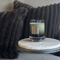 Candle in a glass holder on a marble coaster with a dark cushion in the background