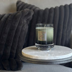 Candle in a glass holder on a marble coaster with a dark cushion in the background