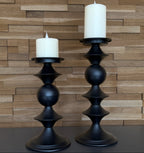 Two black candle holders with white candles against a wooden paneled wall.